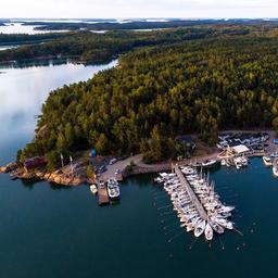 An aerial image of a boat harbour. Lots of boats have docked here, and it is beside a large, green forest.