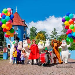 A group of Moomin characters stand in front of a blue house at Moominworld.